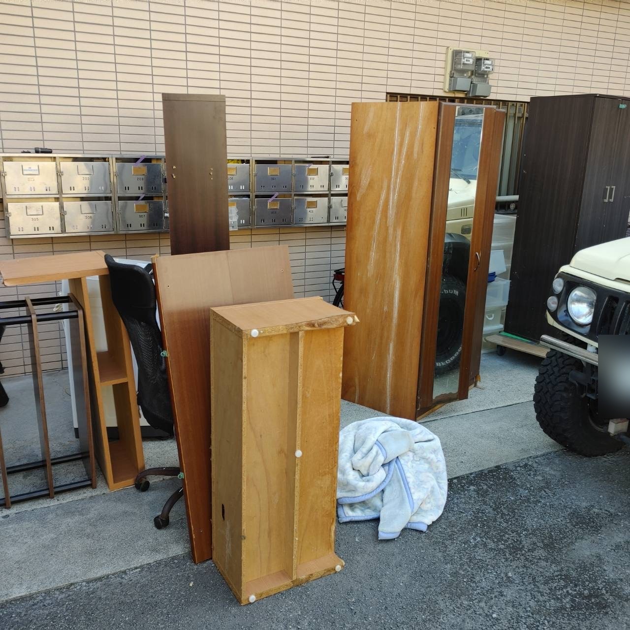 作業前の建物前(鏡付きのクローゼット、本棚、板材、イス、毛布などが並んだ状態)